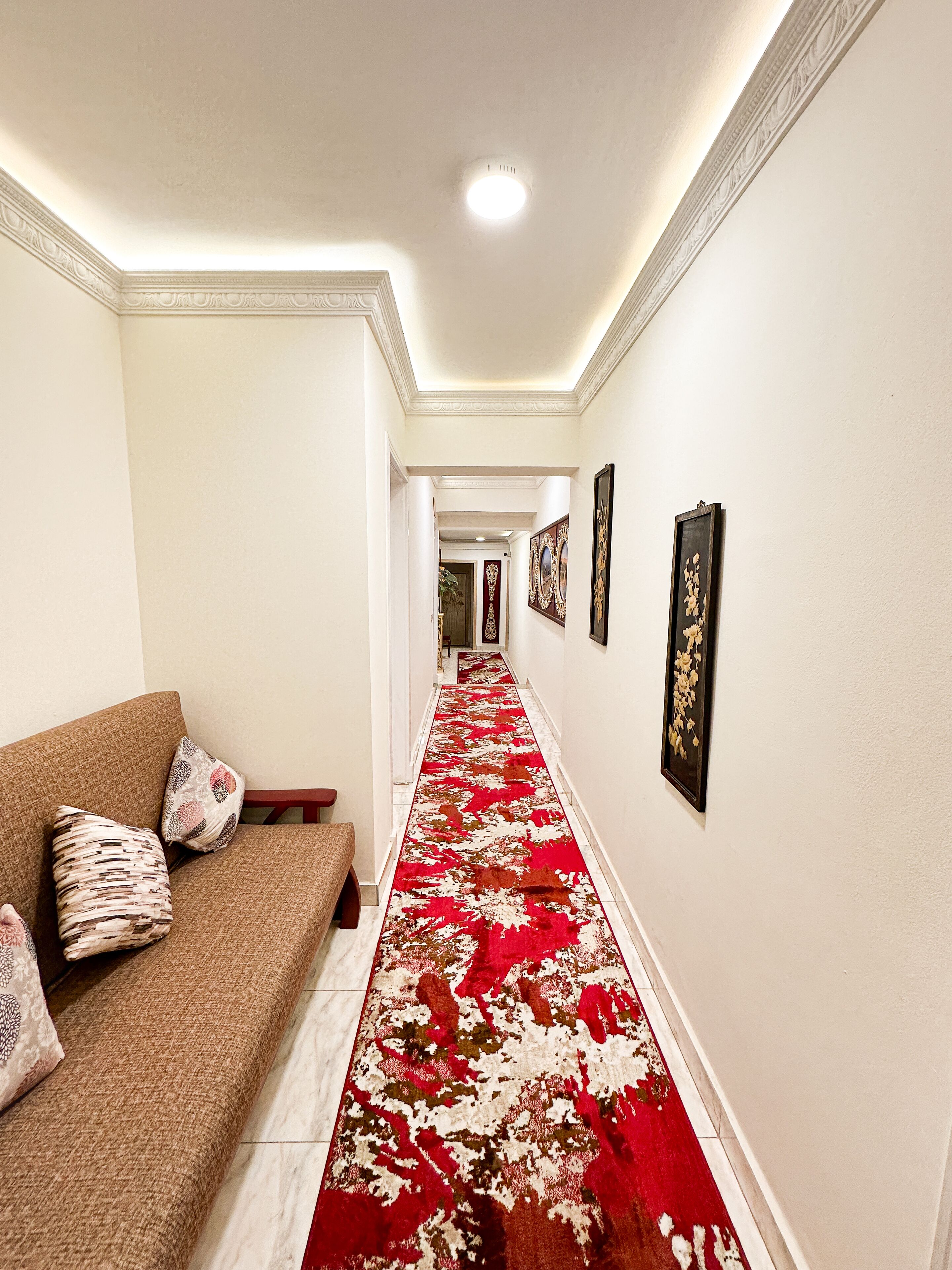 A hallway with a red carpet, a sofa with patterned cushions, and framed artwork on the walls.