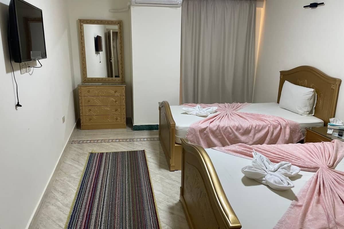 A hotel room with two beds, a TV, a mirror, a dresser, and a window with curtains.