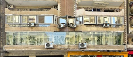 Un edificio de varios pisos con balcones, equipos de aire acondicionado y un escaparate con un letrero rojo.