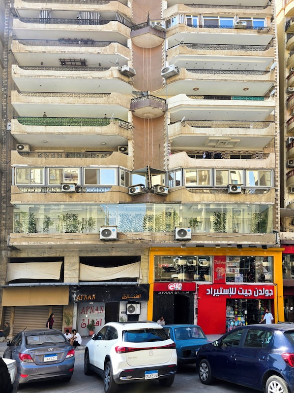 Un edificio de varios pisos con balcones, equipos de aire acondicionado y un escaparate con un letrero rojo.