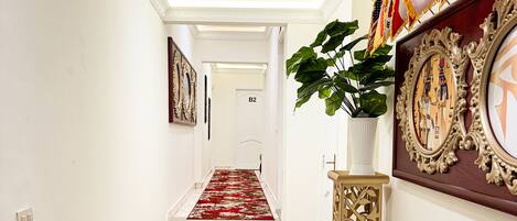 A hallway with a red patterned carpet, a white door labeled B2, and a decorative wall with framed artwork and flags.