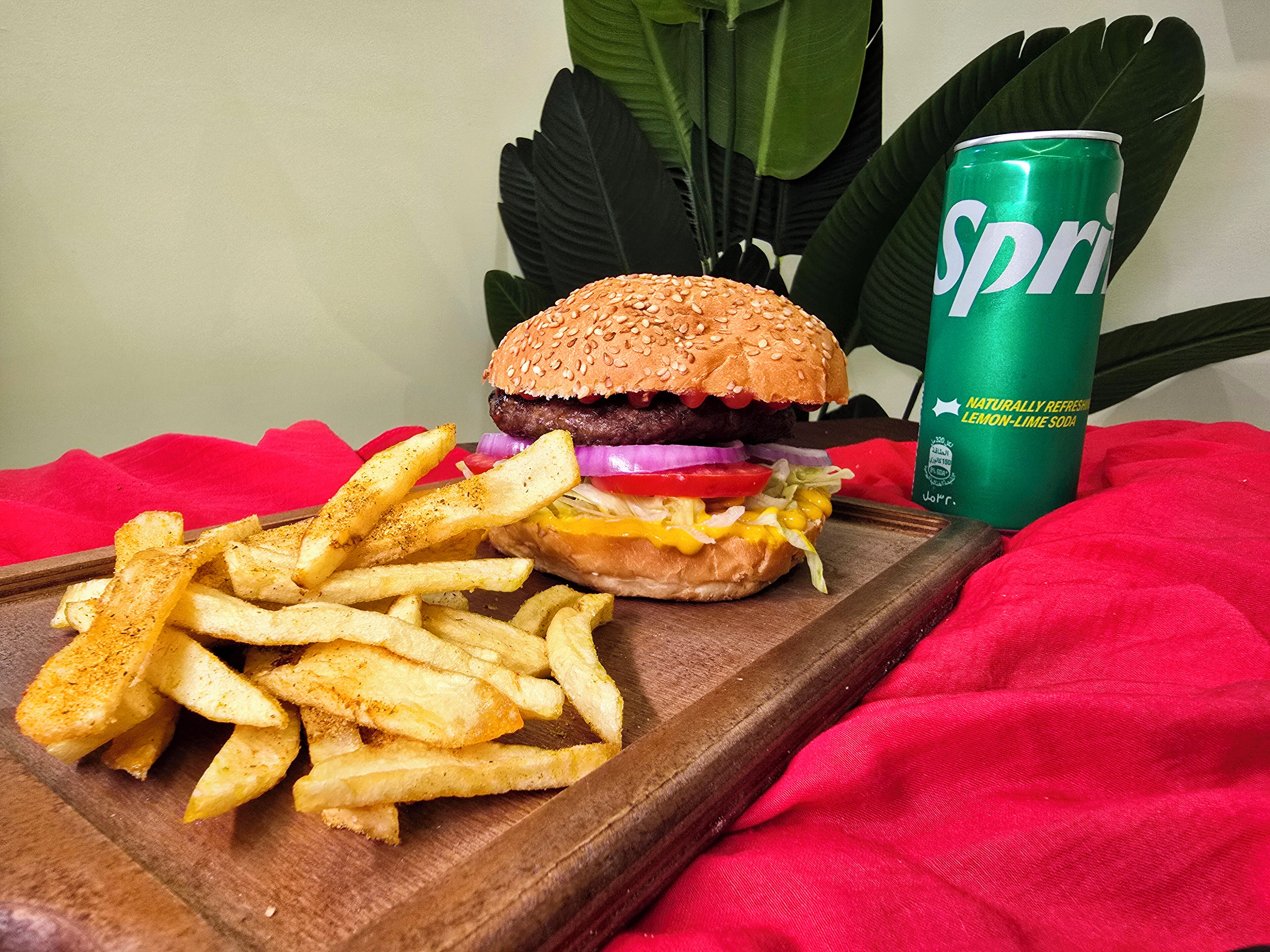 A meal consisting of a burger, fries, and a can of Sprite on a wooden tray with a red cloth.