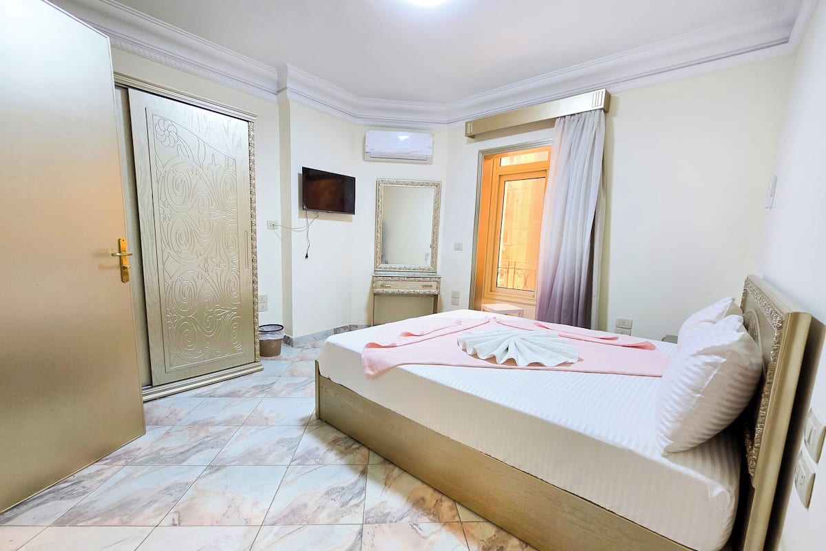 A bedroom with a bed, a wardrobe, a mirror, and a window with curtains.