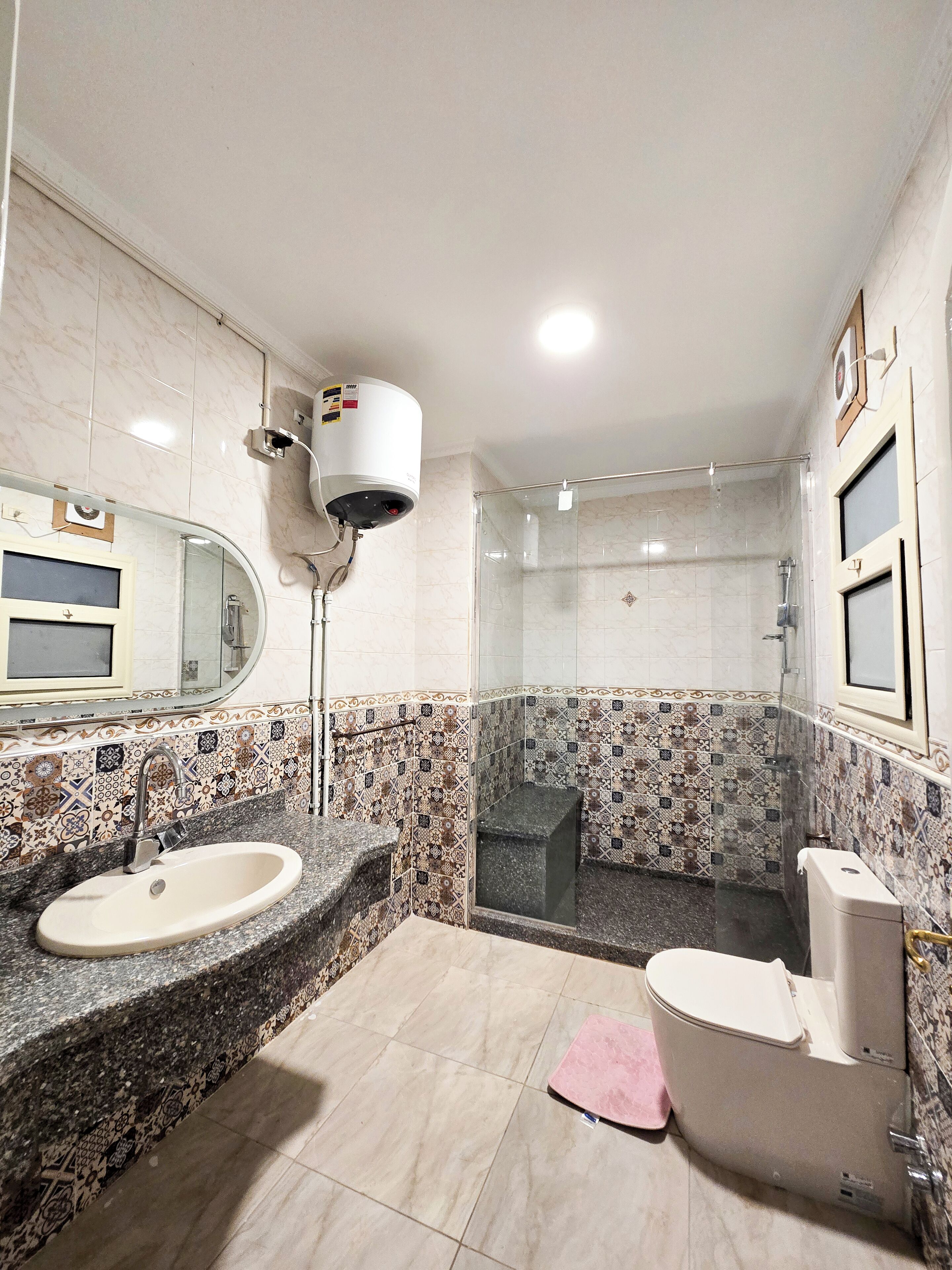 Un baño con lavabo de mármol, inodoro, cabina de ducha y un secamanos de pared.
