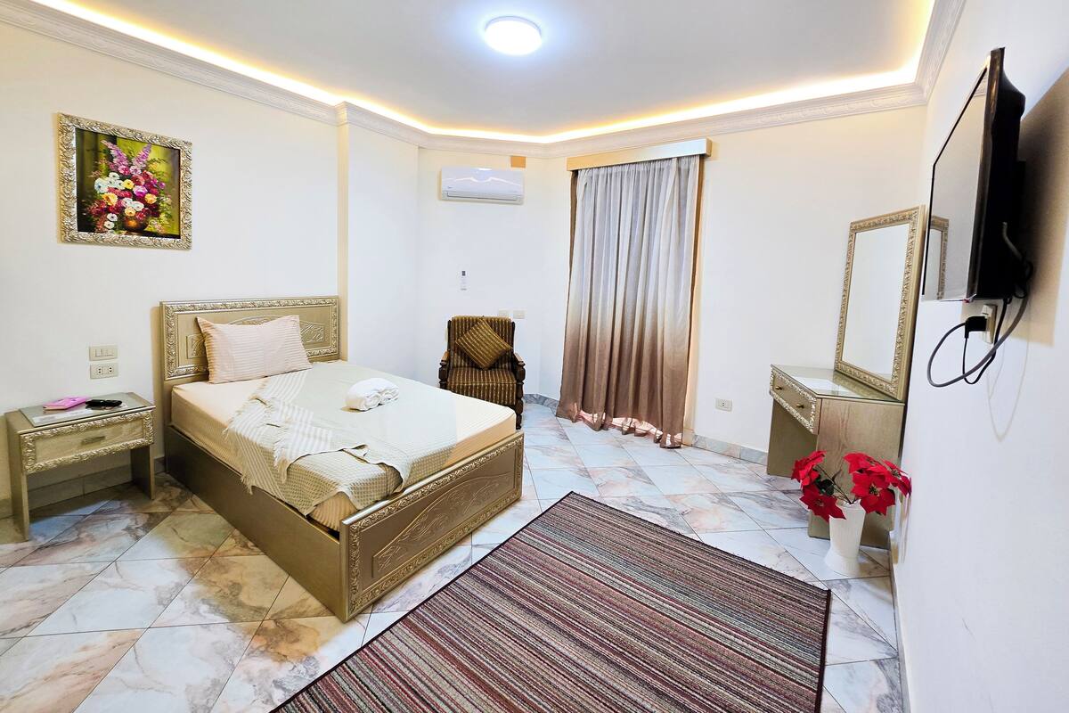 A bedroom with a bed, nightstand, chair, and a television.