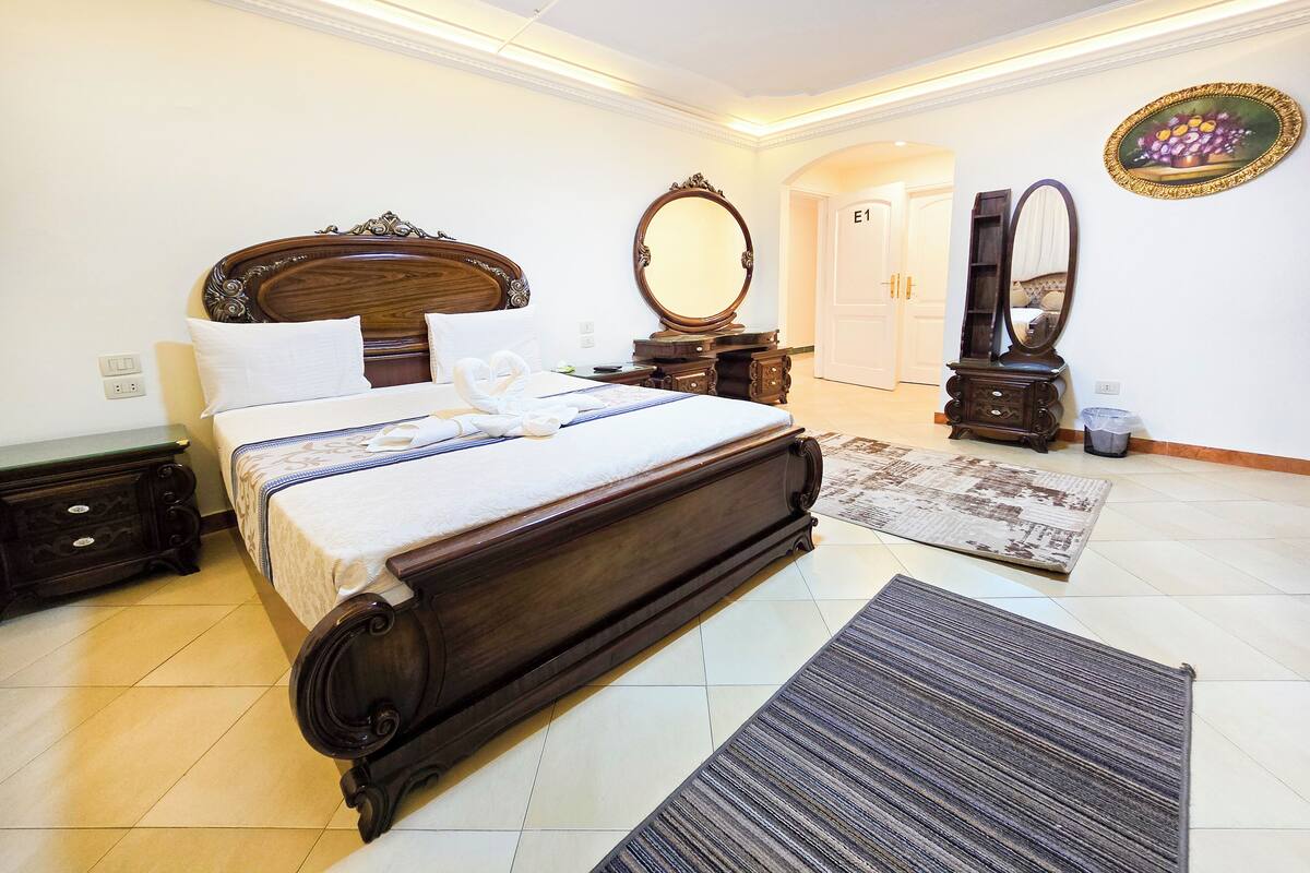 A hotel room with a large bed, a dresser, two mirrors, and a door labeled "F1".