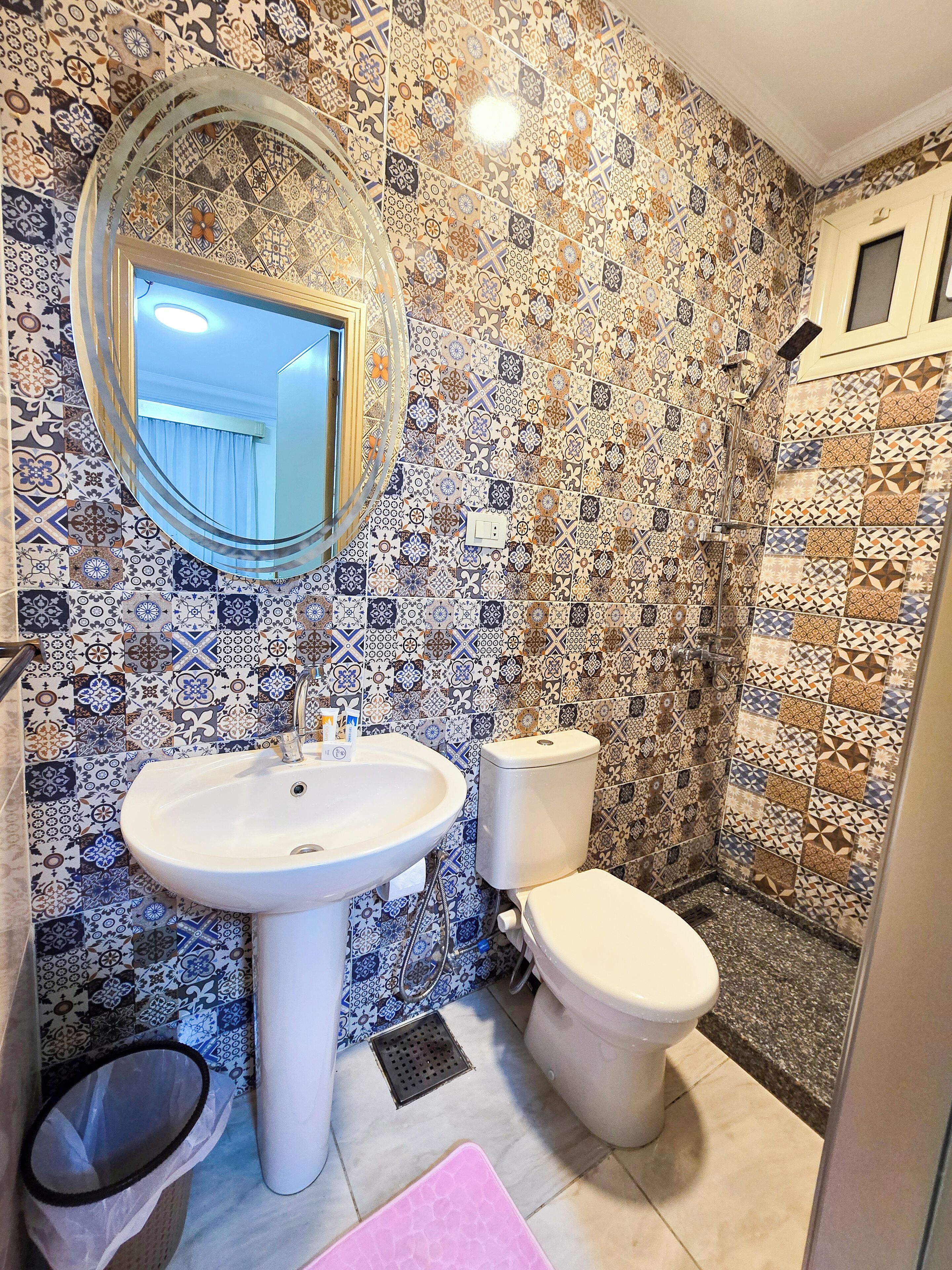 A bathroom with a sink, toilet, and shower. The walls are decorated with patterned tiles.