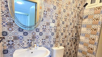 A bathroom with a sink, toilet, and shower. The walls are decorated with patterned tiles.