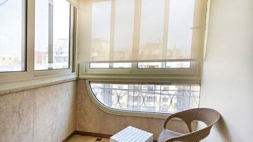Une pièce d’angle avec une vue dégagée grâce à une grande fenêtre, une petite table blanche et un fauteuil en osier.