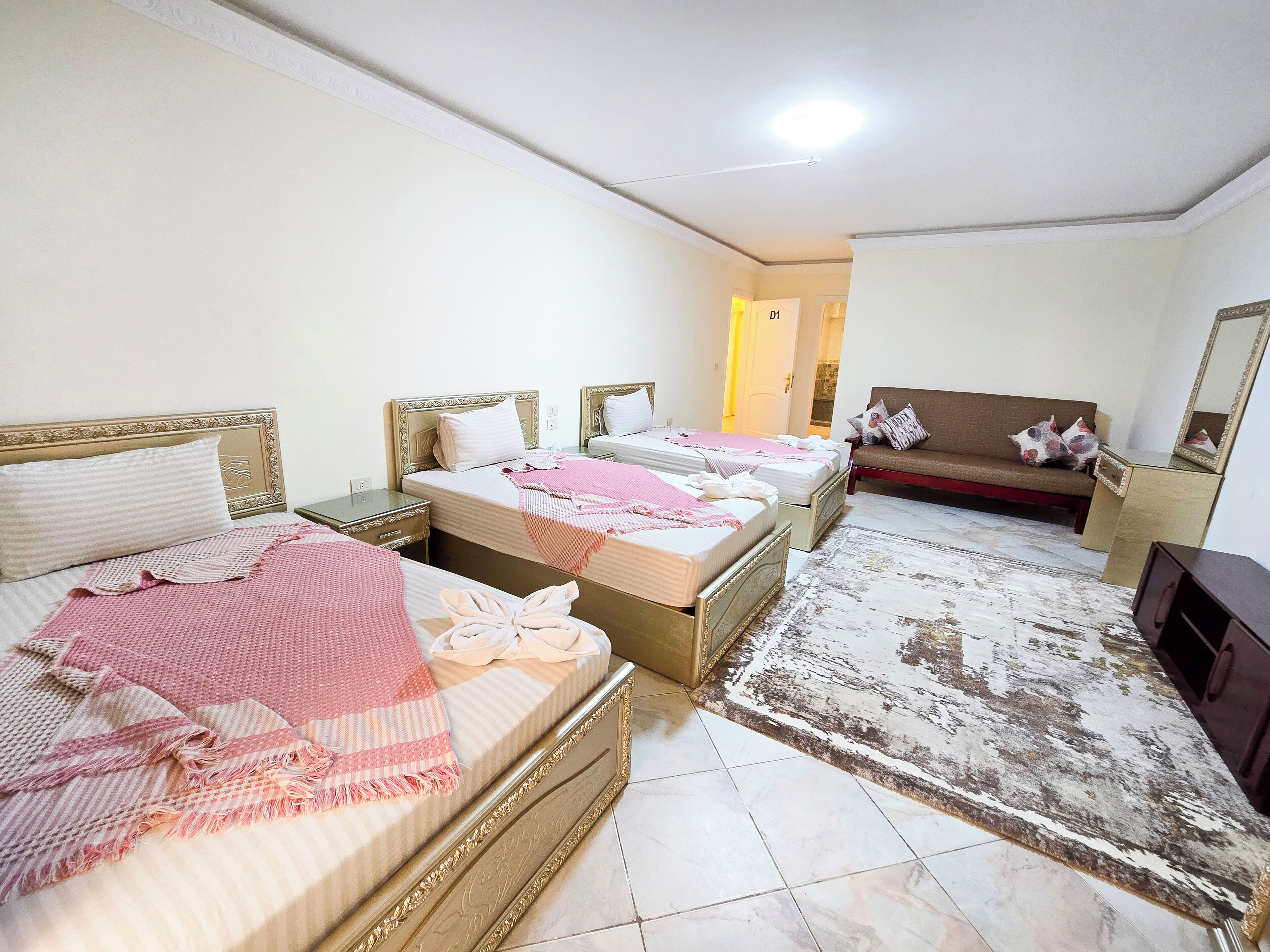 A hotel room with three beds, a sofa, a TV, and a large mirror.