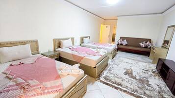 A hotel room with three beds, a sofa, a TV, and a large mirror.