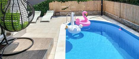 A swimming pool with two inflatable swans, a hanging chair, and a wooden fence.