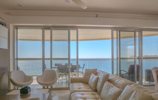 Una sala de estar moderna con un amplio ventanal corredera que da a un balcón con vista al mar.