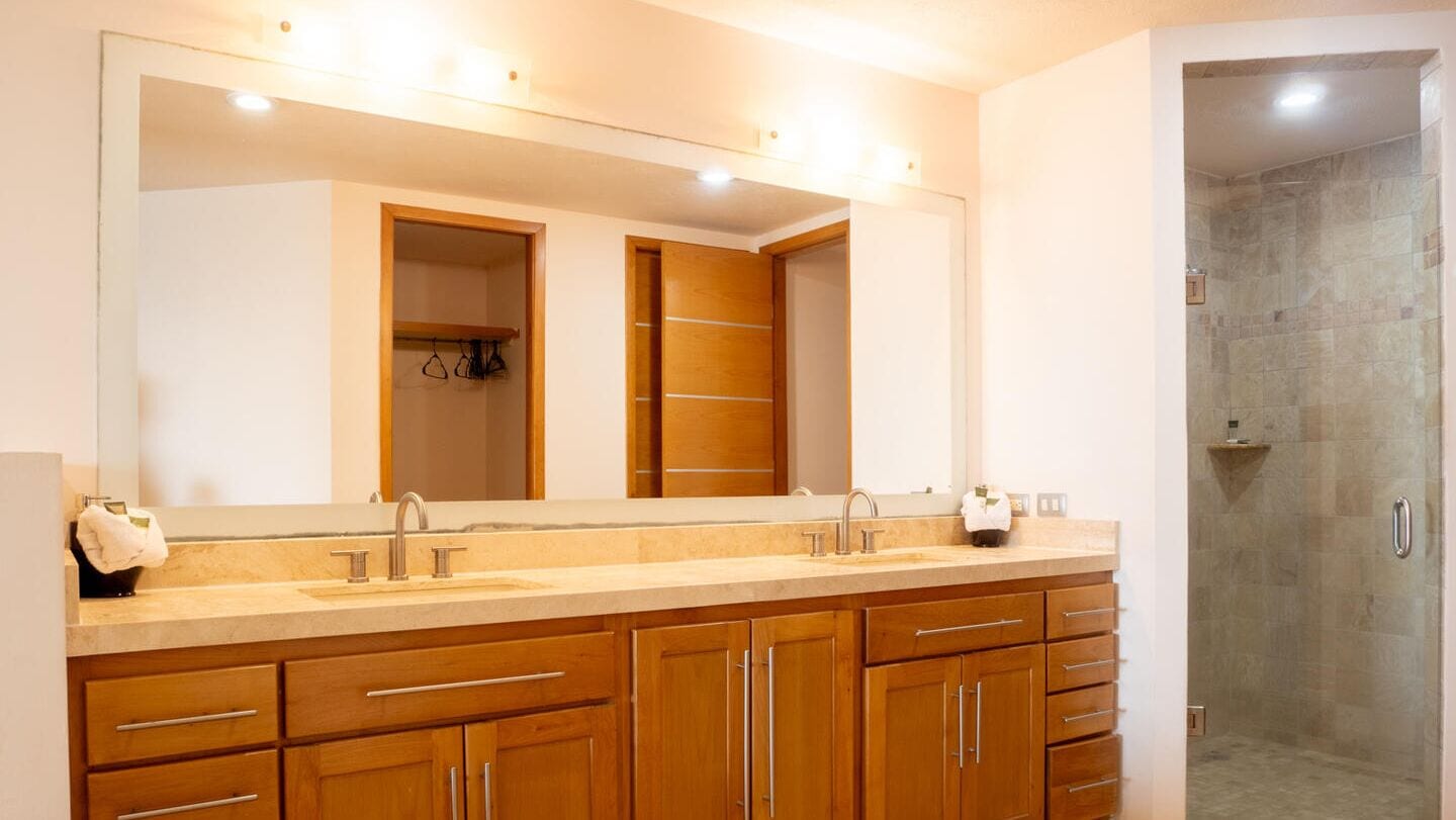 Un baño con un espejo grande, armarios de madera, lavamanos doble y zona de ducha.
