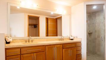 Un baño con un espejo grande, armarios de madera, lavamanos doble y zona de ducha.