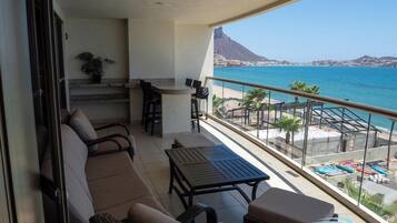 Un balcón con zona de estar, una pequeña mesa y vistas al mar y a la montaña.