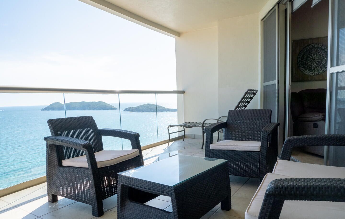 Un balcón con mobiliario de mimbre, una mesa de vidrio y vistas al mar.