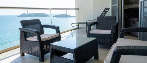 Un balcón con mobiliario de mimbre, una mesa de vidrio y vistas al mar.