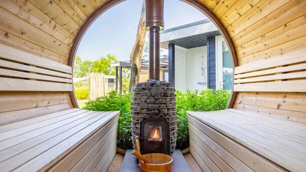 Eine Sauna mit Steinofen, Holzbänken und Blick auf ein modernes Gebäude.