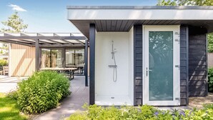 Ein moderner, offener Duschbereich mit Glastür, umgeben von Grünpflanzen und einer überdachten Terrasse.