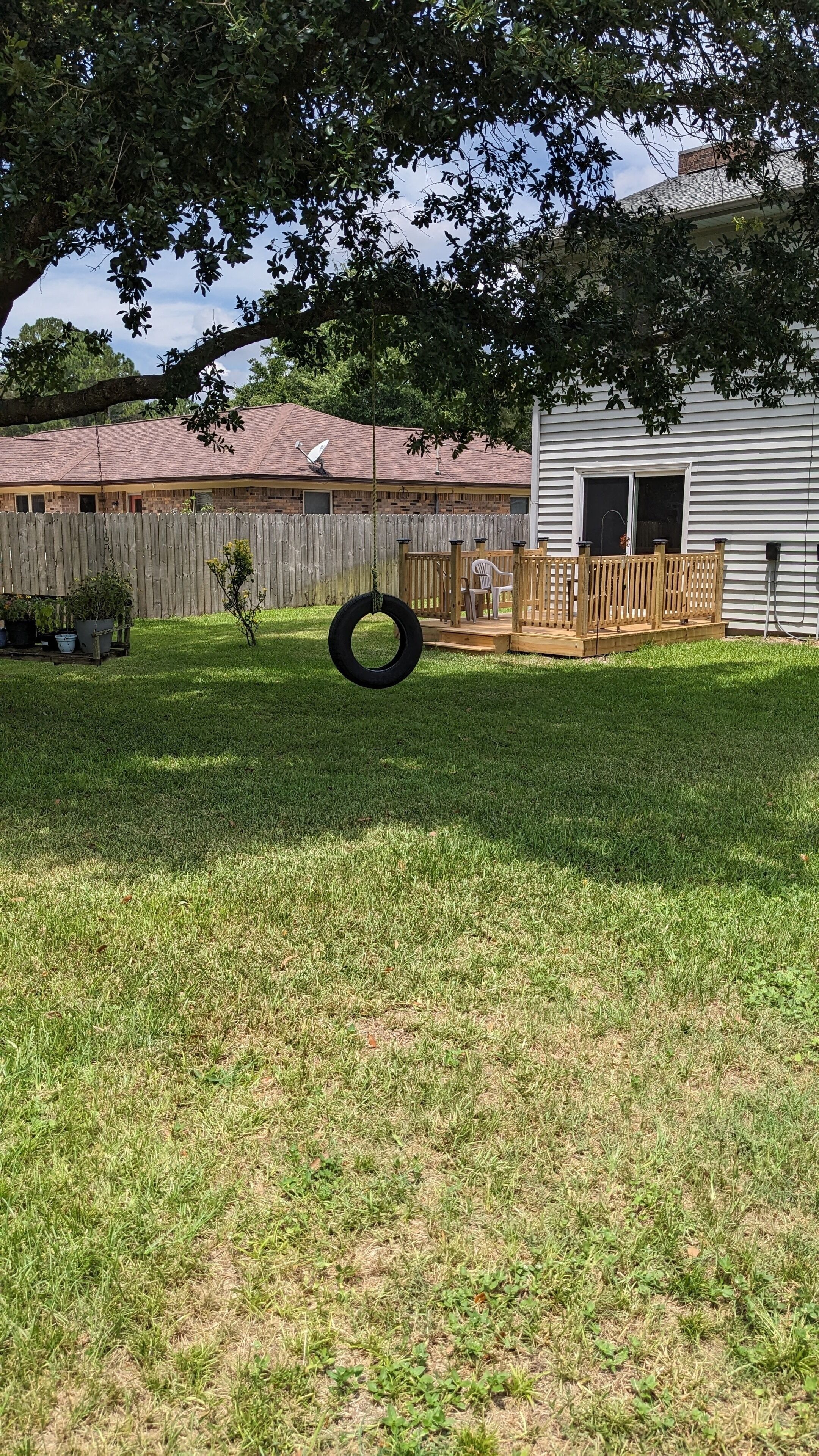 A backyard with a wooden fence, a tire swing, and a house with a satellite dish.