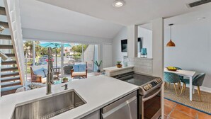 Una cocina moderna con una isla central, un comedor con sillas color turquesa y vistas al exterior.