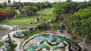 Ein Golfplatz mit Teich, umgeben von üppiger Vegetation und Palmen.