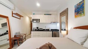 Ein Hotelzimmer mit Bett, kleinem Schreibtisch, Stuhl, Kochnische und Spiegel im Badezimmer.