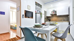 A modern kitchen with white cabinets, a built-in microwave, and a dining area with a white table and two chairs. - GuestHost - Porta Medina Apartment (Napoli)