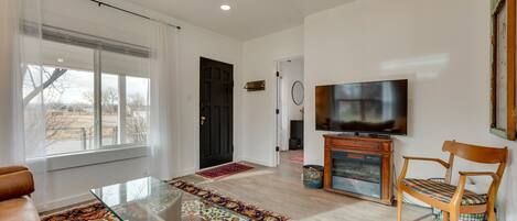 A living room with a glass coffee table, a brown leather sofa, a wooden chair, a television, and a patterned rug.