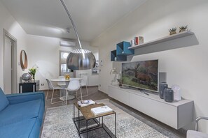 Ein modernes Wohnzimmer mit Sofa, Couchtisch, Fernseher und einem Essbereich mit Stühlen und Tisch.