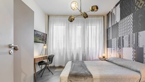 Un dormitorio moderno con cama, escritorio, silla, televisor y pared con diseño.