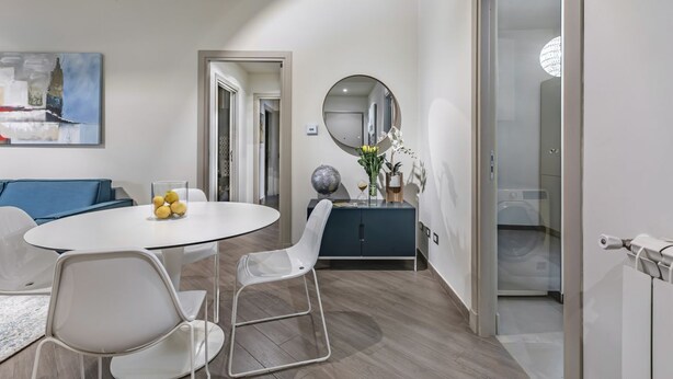 Un interior moderno con una mesa de comedor redonda, sillas blancas, un sofá azul, un armario azul oscuro, un espejo redondo y un globo terráqueo colgado en la pared.