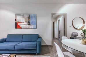 Un salon moderne avec un canapé bleu, une table ronde surmontée d’un globe terrestre et un tableau accroché au mur.