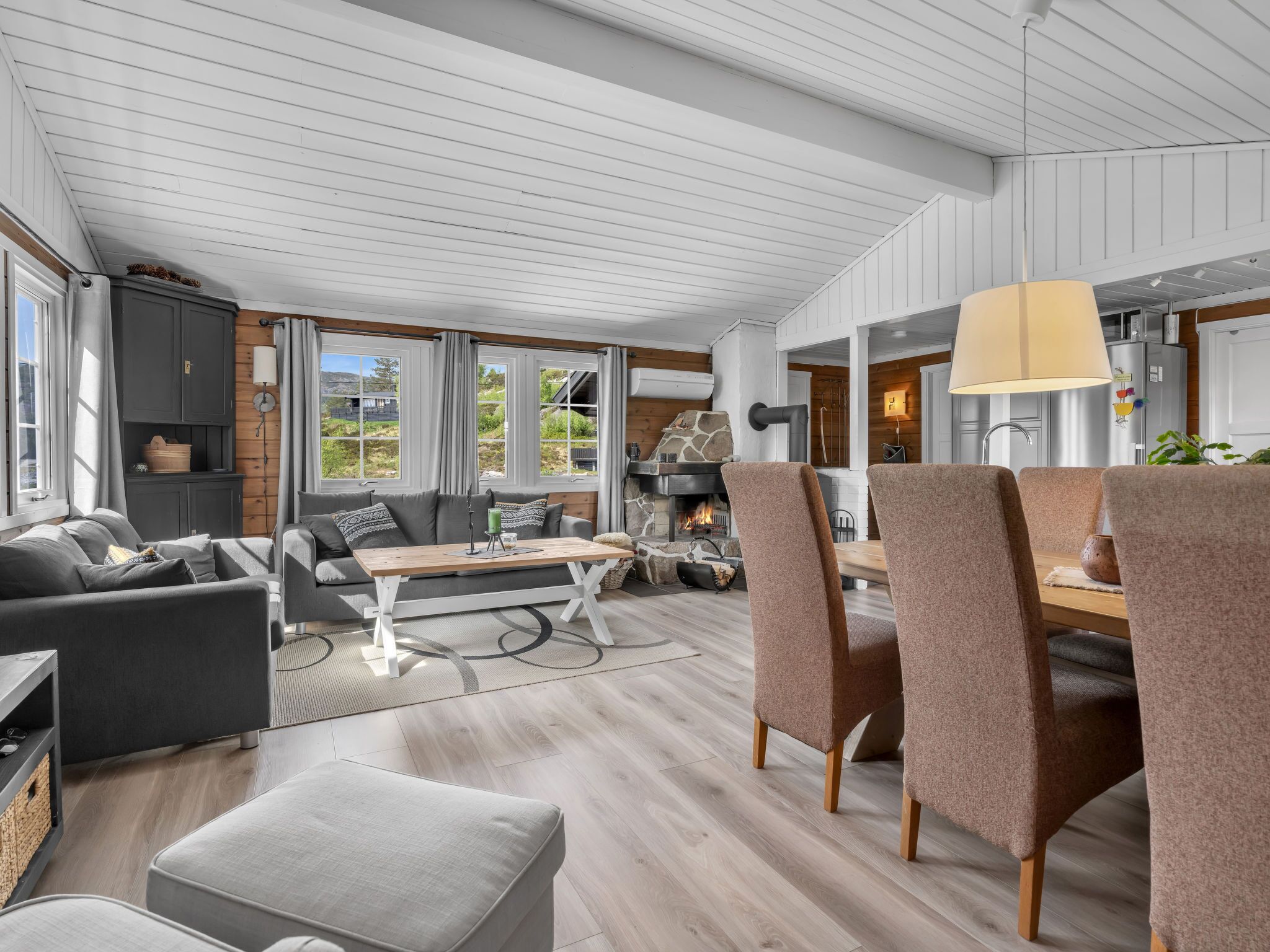 A modern living room with a fireplace, a dining area with chairs, and a kitchen visible through an open door.