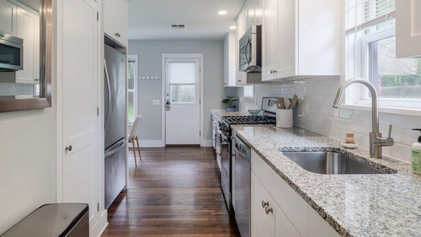 A kitchen with white cabinets, a stainless steel refrigerator, a granite countertop, and a window with blinds.