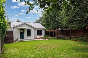 A single-story house with a sloped roof, a front porch with a bench, and a fenced backyard. - Quintessential Zilker Bungalow (Austin)