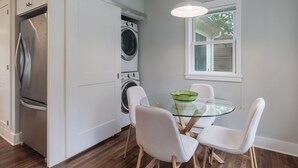 A compact kitchen with a refrigerator, washing machine, and a glass table with chairs.