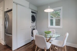 A compact kitchen with a refrigerator, washing machine, and a glass table with chairs. - Quintessential Zilker Bungalow (Austin)