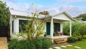 A single-story house with a green door, a porch with a bench, and a small garden with stepping stones leading to the entrance.