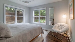 A bedroom with a bed, a chair, a ceiling fan, and large windows.