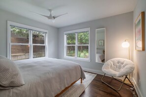 A bedroom with a bed, a chair, a ceiling fan, and large windows. - Quintessential Zilker Bungalow (Austin)