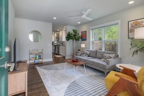 A modern living room with a grey sofa, a coffee table, a TV, and a bookshelf. - Quintessential Zilker Bungalow (Austin)