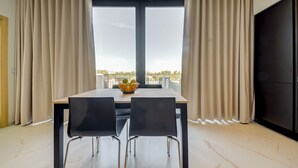 Un espace de salle à manger moderne avec une table et des chaises, un saladier rempli de fruits et une vue dégagée grâce à de grandes fenêtres.
