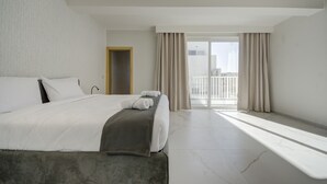 Une chambre d’hôtel moderne avec un grand lit, un banc et une vue sur la ville depuis le balcon.