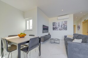 A modern living room with a dining table, grey sofa, and a painting on the wall. - Two Bedroom Penthouse - Jacuzzi (Swieqi)