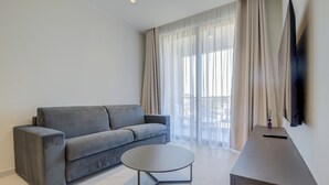 Un salon moderne avec un canapé gris, une table basse ronde et un téléviseur posé sur un meuble.
