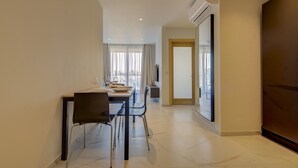 Une chambre d’hôtel moderne dotée d’un coin repas avec une table dressée pour quatre personnes, d’un canapé et d’un téléviseur fixé au mur.