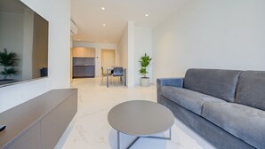 Un salon moderne avec un canapé gris, une petite table ronde et un coin repas comprenant une table et des chaises.