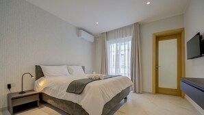 A modern bedroom with a large bed, bedside tables, a TV, and a window with curtains. - Three Bedroom Suite - Jacuzzi (Swieqi)